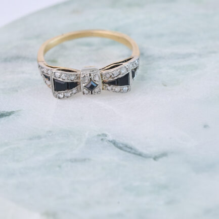 ANILLO ART DÉCO EN FORMA DE LAZO REALIZADO EN ORO AMARILLO Y VISTAS DE PLATINO ENGARZANDO DIAMANTES Y ÓNIX.